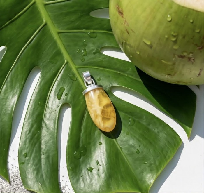 Sea Treasure Prehistoric Authentic Butterscotch Baltic Amber .925 Sterling Silver beautifully handcrafted Pendant - Amber pendant on leaf next to coconut, top-down view.