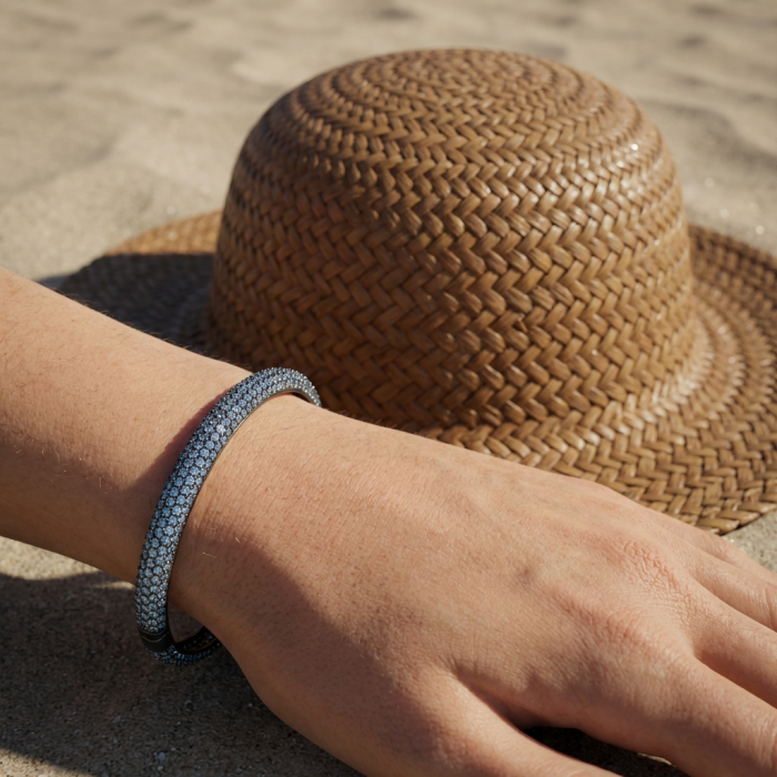 Precious Genuine Pave 22.5 carat White Topaz black rhodium over .925 Sterling Silver handcrafted Bracelet - Worn on hand with brown woven hat in background on sandy surface.