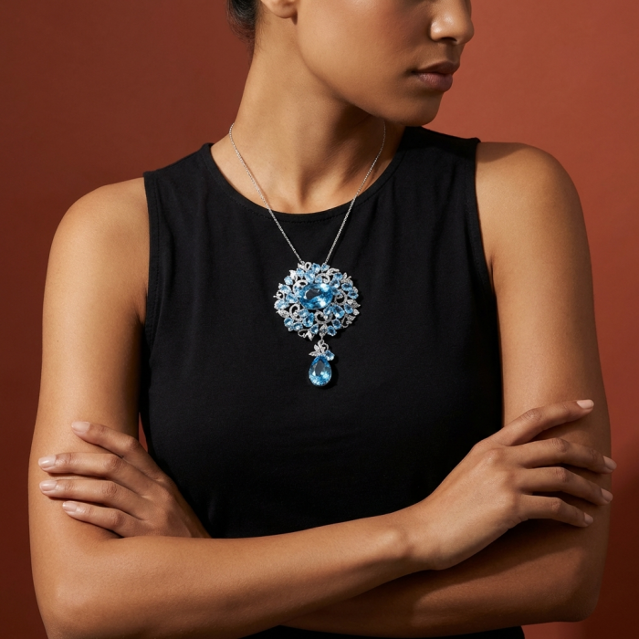 An exuberantly Large 75.5 grams Vintage style Swiss Blue Topaz .925 Sterling Silver DIPPED IN RHODIUM handmade LARGE Pendant - Brooch - Model wearing large Swiss Blue Topaz necklace, arms crossed, front view.
