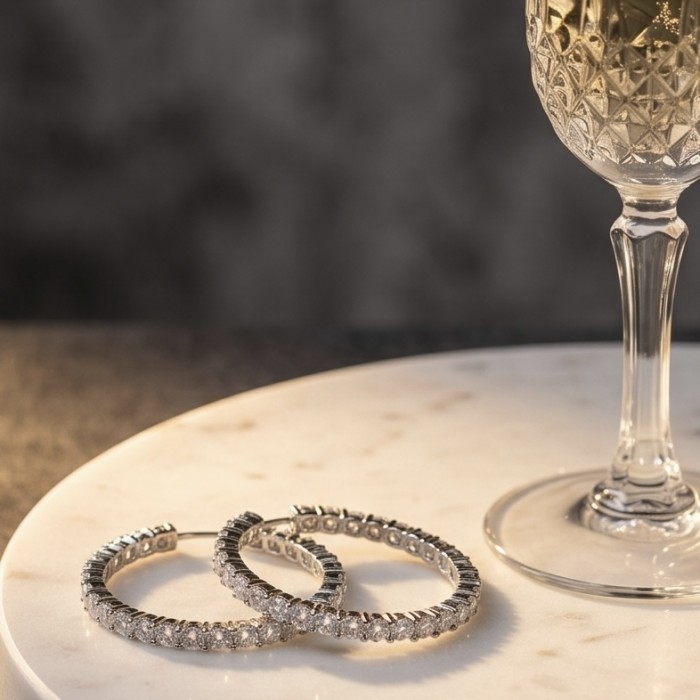 INSIDE - OUT Huge 1 5/8 inches long White Topazrhodium over .925 Sterling Silver handmade Hoop Earrings - Earrings on marble surface beside a wine glass, angled side view.