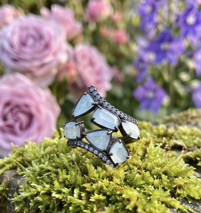 Blue Cascade 7.5 carat Rainbow Moonstone black rhodium over .925 Sterling Silver handmade ring s. 7 - Blue Cascade ring on moss with pink and purple flowers in background.