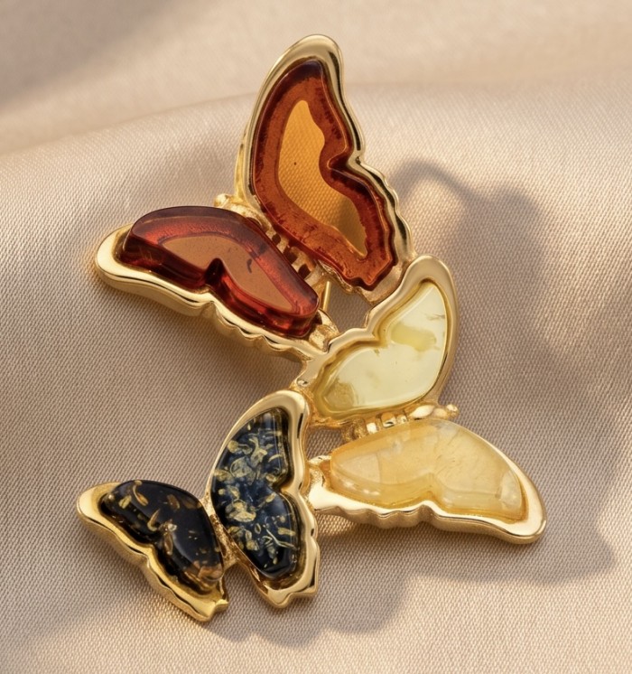 Golden Butterflies Authentic carved Baltic Amber 18K Gold over .925 Sterling Silver handcrafted pendant - Golden butterfly brooch with amber stones, top view, on fabric background.